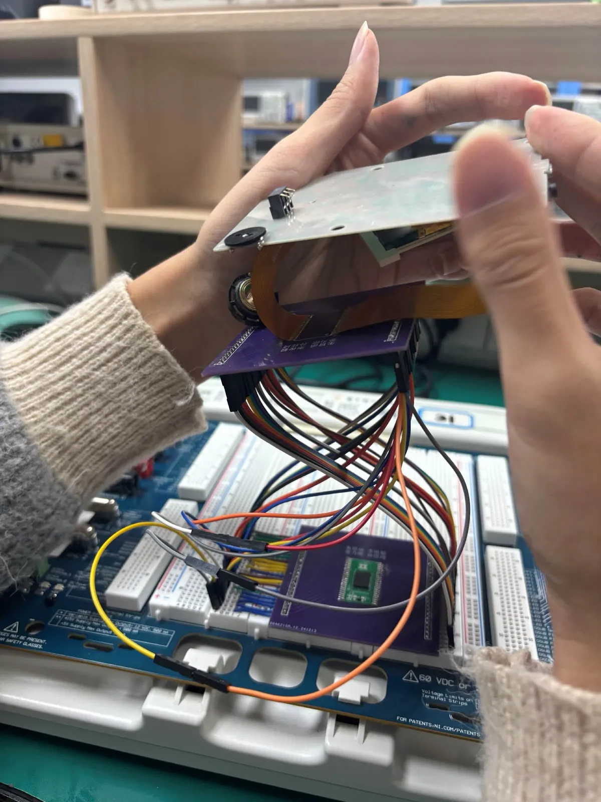 The full rig. The two purple boards are ours, fabricated from our own files, with the chip soldered on; headers plug into an NI ELVIS breadboard, dupont wires carry the signals to the ribbon cable, and that runs back to the console motherboard being held.